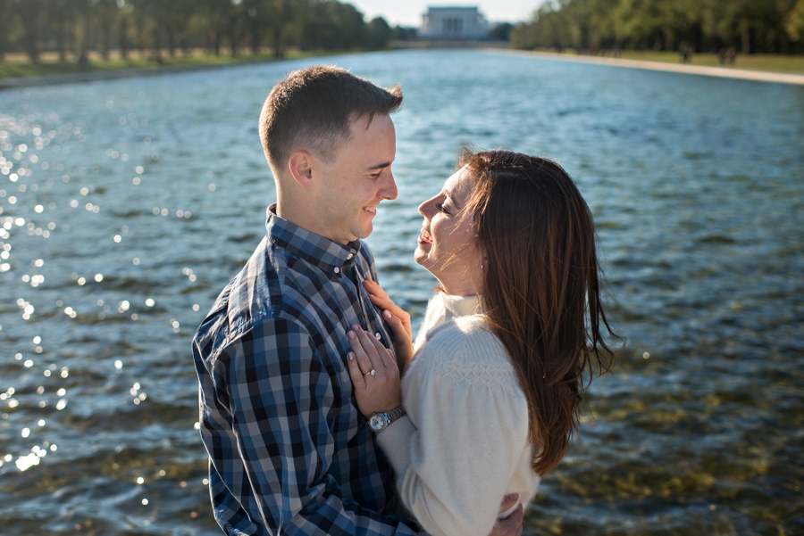 A newly engaged Navy couple hug in front of the Lincoln Memorial Reflecting Pool for their DC Engagement Session.